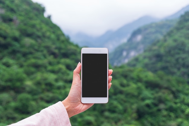 Main de femme tenant un téléphone intelligent au parc naturel en plein air, entreprise de technologie d'espace copie et concept de vacances nature voyage.