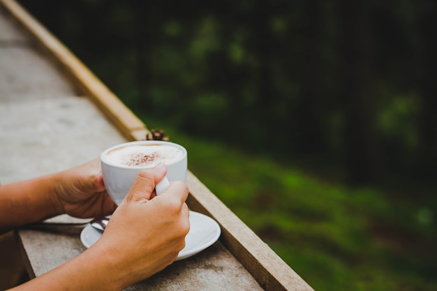 Main de femme tenant un verre de café dans le jardin.