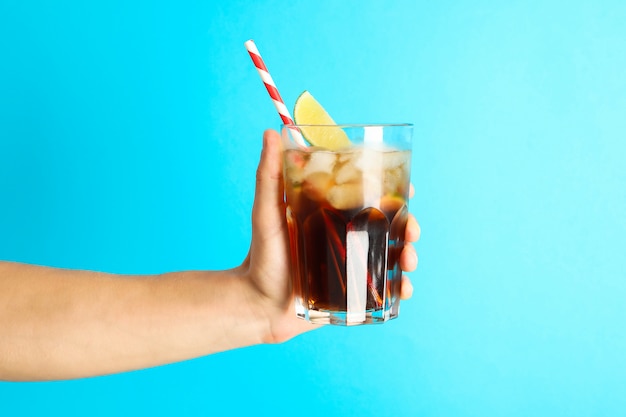 Main de femme tenant un verre de cola de glace, tubule et tranche de citron vert