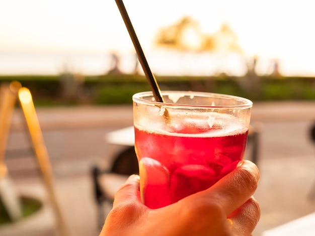 Main de femme tenant un verre de sangria contre le coucher du soleil