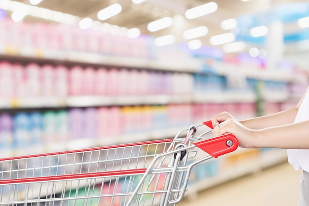 Main de femme tenir un caddie rouge vide avec fond intérieur d'étagères de supermarché