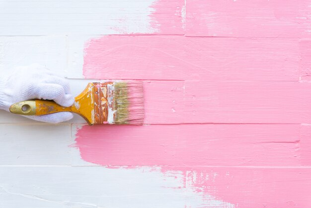 Main femme tenue brosse peinture couleur rose sur une table en bois blanche