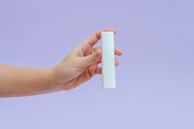 La main de la femme tient une bataille de crème de tube blanc pour les produits cosmétiques isolés sur fond lilas