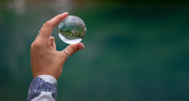 La main d'une femme tient une boule de verre sphérique dans le contexte d'un magnifique lac de montagne