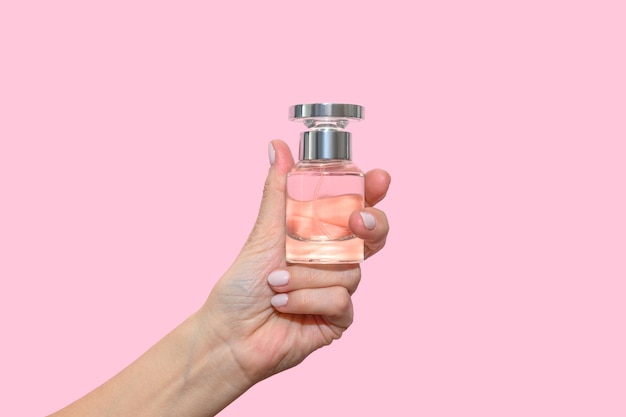 La main d'une femme tient une bouteille de parfum en verre sur fond rose