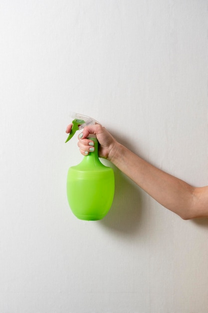 La main d'une femme tient une bouteille en plastique avec un vaporisateur vert sur fond gris. Le concept de soins à domicile et de nettoyage.