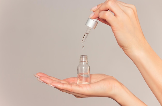 La main d'une femme tient une bouteille transparente de liquide cosmétique et fait couler une pipette dans la bouteille