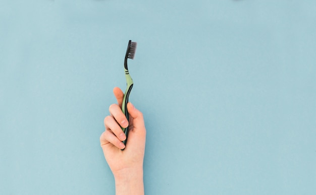 La main de femme tient une brosse à dents sur bleu