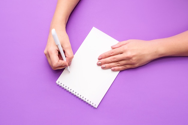 La main d'une femme tient un cahier avec des feuilles blanches sur fond clair. Une place pour le texte, une vue d'en haut. Mise à plat