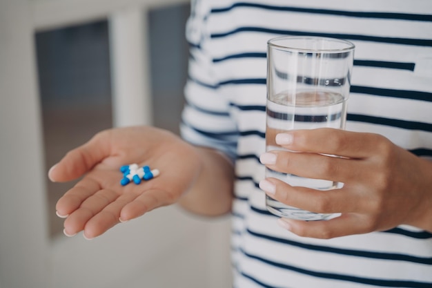 La main de la femme tient des capsules blanches et bleues et un verre d'eau La dame va prendre des médicaments