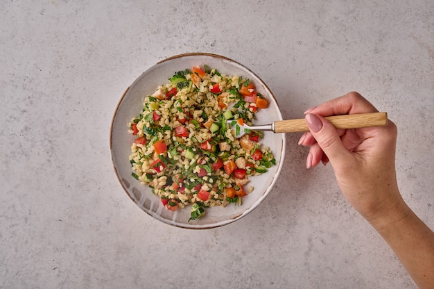 Main de femme tient une fourchette avec une salade de taboulé dans un bol sur fond clair copie espace vue de dessus