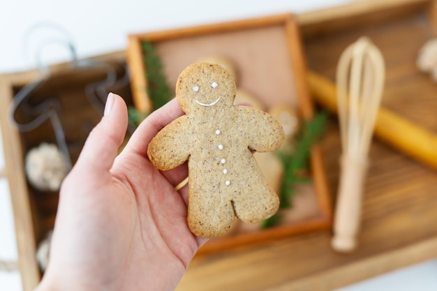 La main d'une femme tient un homme en pain d'épice Cuisiner du pain d'épice à la maison se trouve sur un plateau en bois Concept de vacances