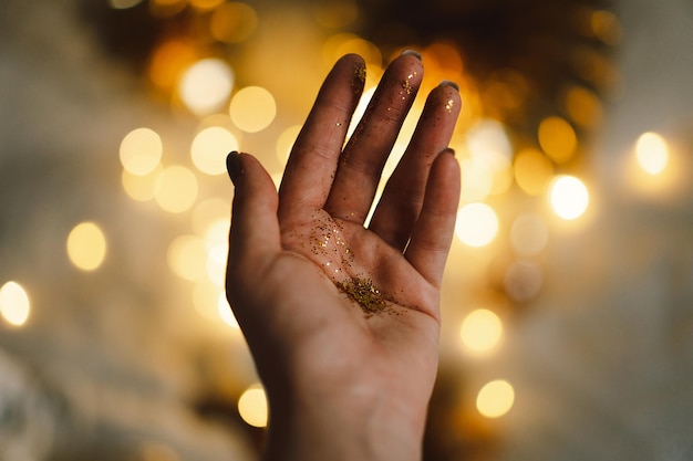 Photo la main d'une femme tient des paillettes d'or sur fond festif avec des lumières dorées ambiance de noël et hiver atmosphérique concept de célébration de bonne année