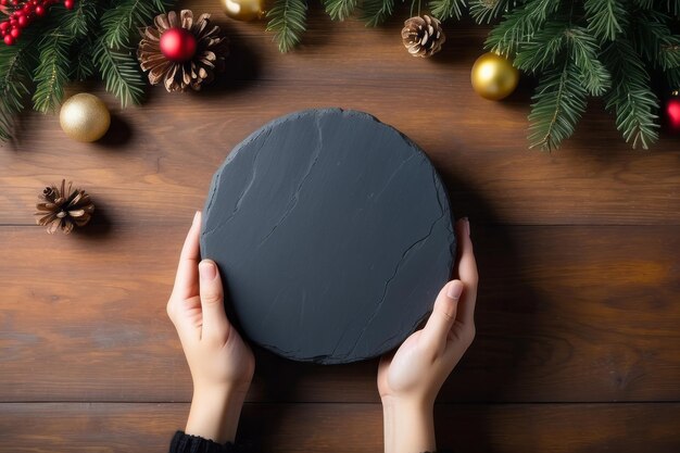 Photo la main de la femme tient la pierre ronde en ardoise noire sur fond de bois avec une décoration de noël