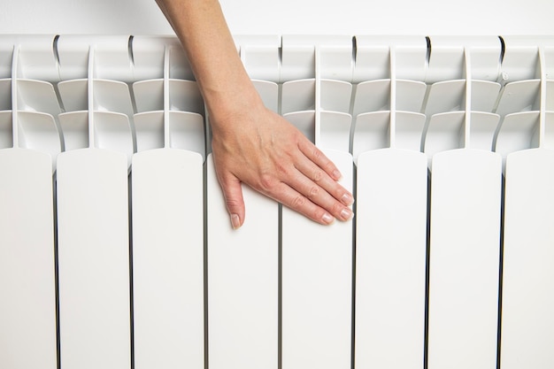 La main d'une femme tient à un radiateur blanc Concept de chauffage