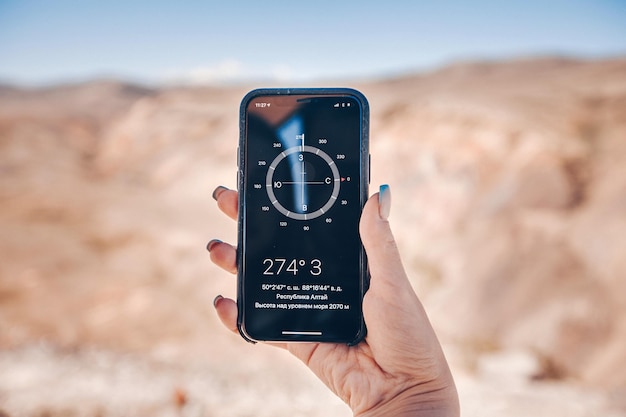 La main d'une femme tient un smartphone avec la boussole incluse. Arrière-plan flou de collines rocheuses. Un repère dans l'espace montagnard pour voyager.