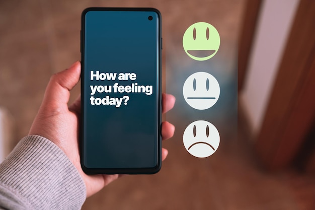 La main d'une femme tient un smartphone tout en choisissant un sourire heureux à l'écran sur ce qu'elle ressent