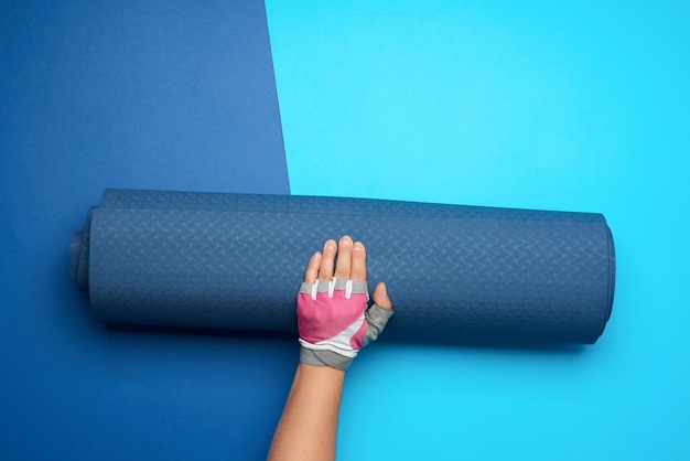 Photo la main de la femme tient un tapis de sport en néoprène enroulé sur un fond bleu