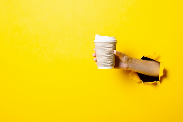 La main de la femme tient une tasse en papier avec du café fermé par une bosse sur un fond jaune vif