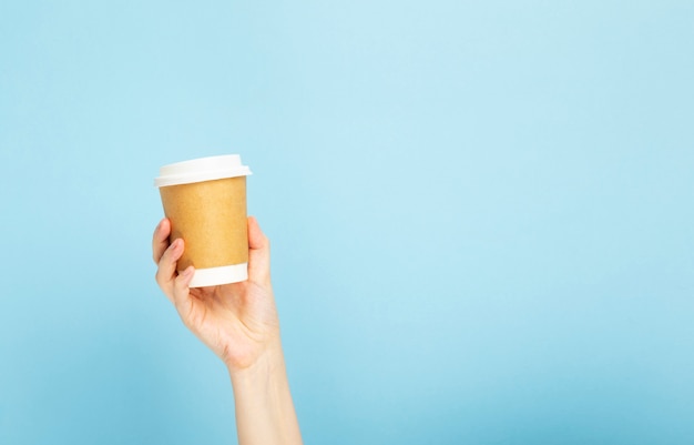 Main de femme tient une tasse en papier avec du café sur fond bleu.