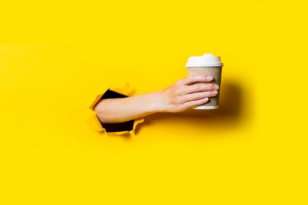 La main de la femme tient une tasse de papier avec du café sur fond jaune vif