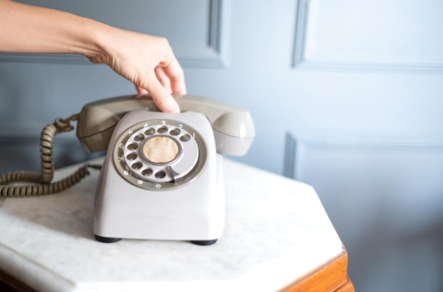 La main de la femme tient le vieux téléphone gris classique sur la table en bois classique de la pièce intérieure