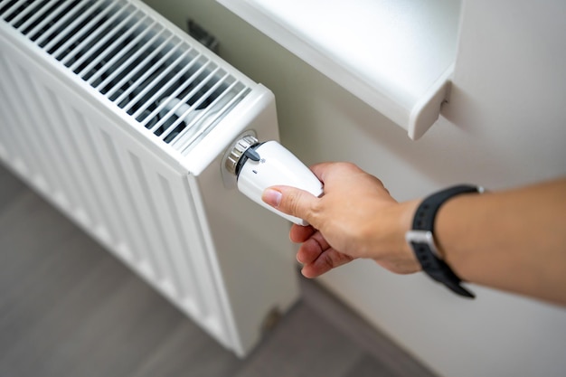 La main d'une femme tourne le bouton de chauffage de la batterie chauffage dans un appartement à la maison prix du chauffage