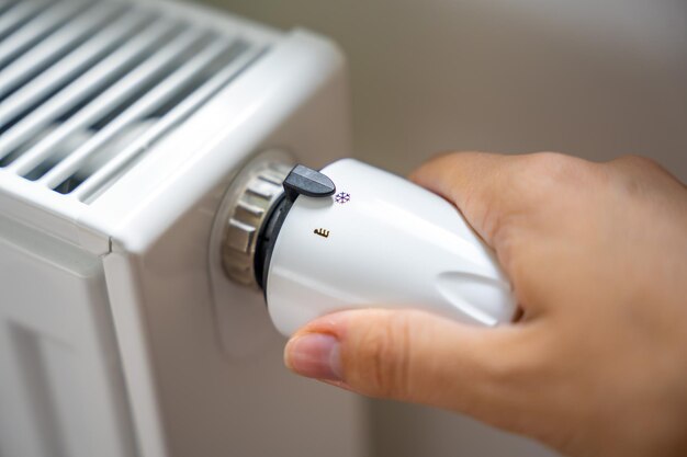 La main d'une femme tourne le bouton de chauffage de la batterie chauffage dans un appartement à la maison prix du chauffage