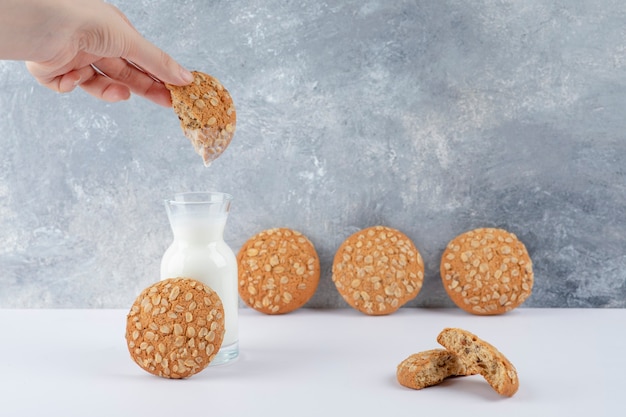 Main de femme trempant un biscuit à l'avoine dans un pichet en verre de lait.