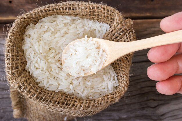 Main de femme utilisent cuillère en bois cueillette riz au jasmin de petit sac sur la table en bois.
