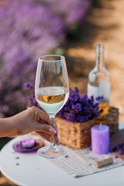 Main de femme avec un verre de vin blanc sur fond de champs de lavande en Provence France Lignes de buissons de fleurs violettes