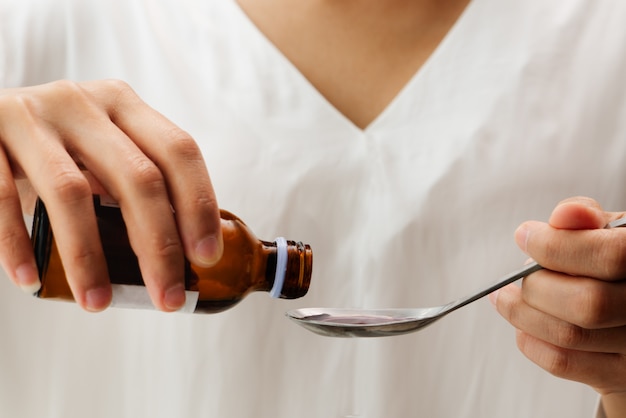 Main femme versant un médicament ou un sirop contre la toux d&#39;une bouteille à la cuillère. concept de santé