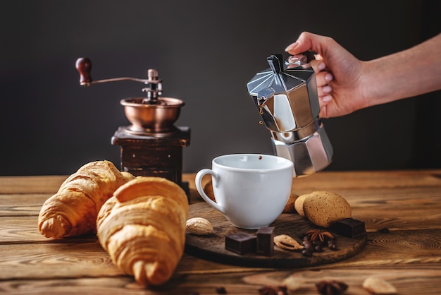 La main d'une femme verse du café noir chaud frais d'une cafetière geyser