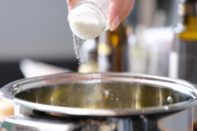 Une main de femme verse du sel fin dans une casserole. Concept de contrôle du sel de cuisine