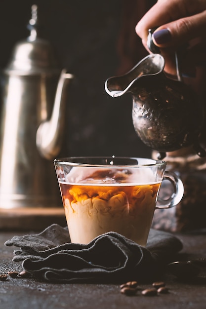 Main de femme verser le lait dans une tasse en verre de café