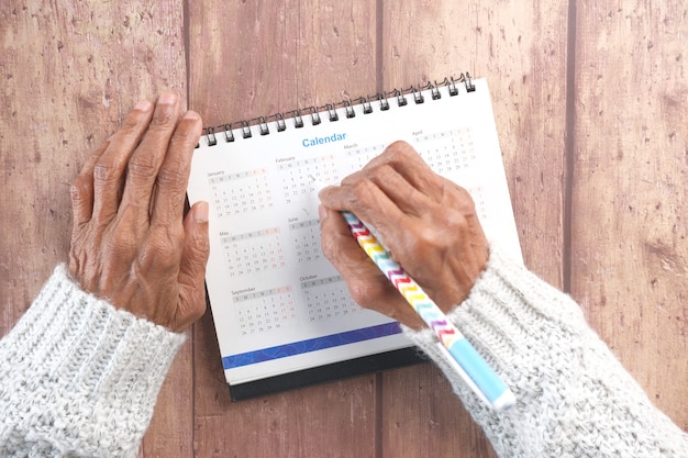 Main de femmes âgées avec un cercle de stylo sur la date du calendrier 2021 sur un mur en bois