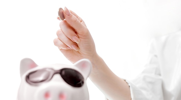 La main des femmes de haut en bas met une pièce de monnaie dans le cochon tirelire avec des lunettes. photo de haute qualité