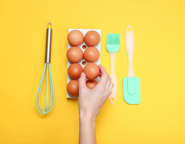 La main des femmes prenant l'oeuf de poule du plateau d'oeufs sur jaune.