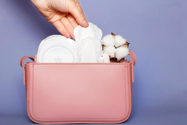 La main des femmes sort le protège-slip du sac cosmétique rose avec des tampons et des serviettes hygiéniques féminines