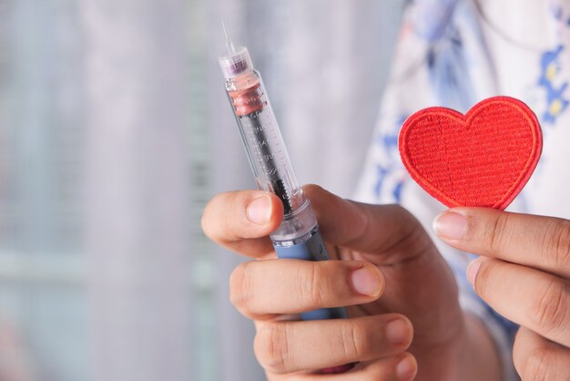 Main de femmes tenant stylos à insuline et symbole du coeur avec espace de copie.