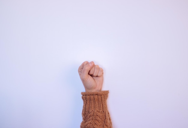 Main fermée de femme avec un pull marron sur fond blanc