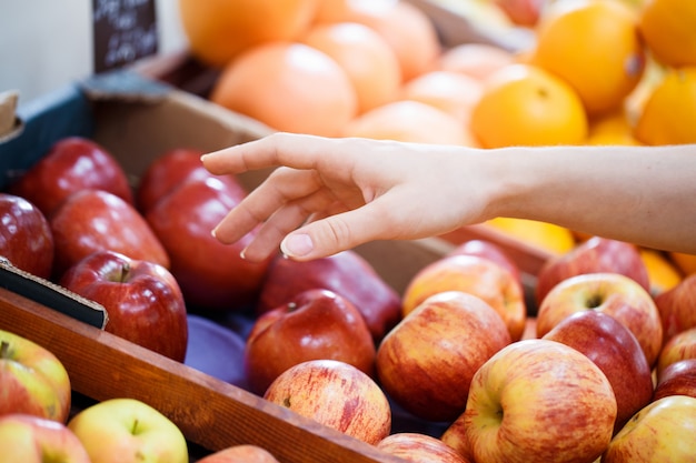 La main fermée sélectionne des pommes sur l'étagère du magasin de légumes