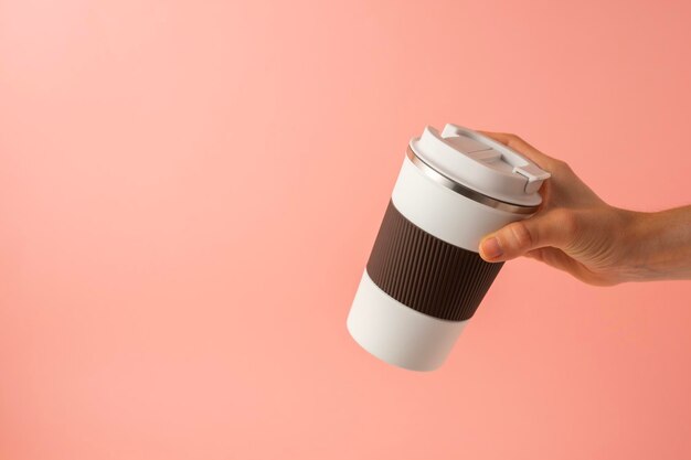 Photo la main d'une fille prenant un thermos de café sur un espace de copie de fond rose