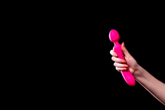 La main de la fille tient un masseur rose pour le sexe sur un fond noir isolé Vibromasseur pour la masturbation Gode pour la stimulation Image pour sex-shop