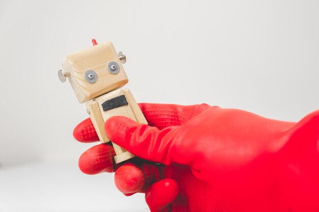 Photo une main avec un gant en caoutchouc rouge saisit un petit robot en bois jouet concept de production à zéro déchet