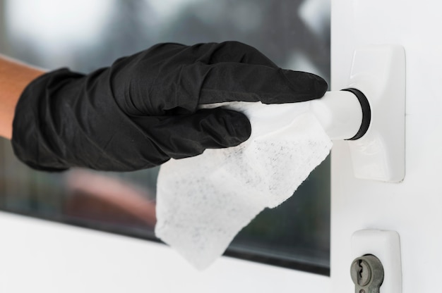 Main avec gant chirurgical désinfectant la poignée de porte