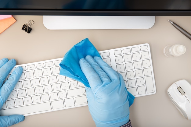 Main avec un gant de protection nettoyant un clavier avec un désinfectant. concept de prévention. Vue de dessus