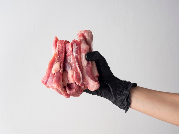 Une main gantée de noir tient un morceau de viande crue sur un fond clair.