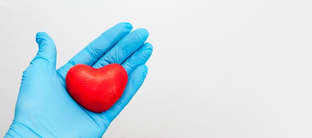 Une main gantée tient un coeur rouge. Concept de soins médicaux. Espace copie