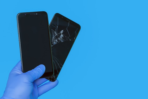 Photo la main gantée tient le nouveau smartphone remplaçant un vieux smartphone cassé avec un écran fissuré sur fond bleu, le concept d'un service de réparation de smartphone de qualité